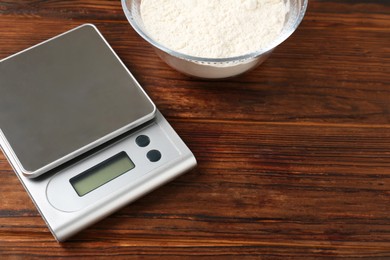 Photo of Electronic kitchen scale and bowl with flour on wooden table. Space for text