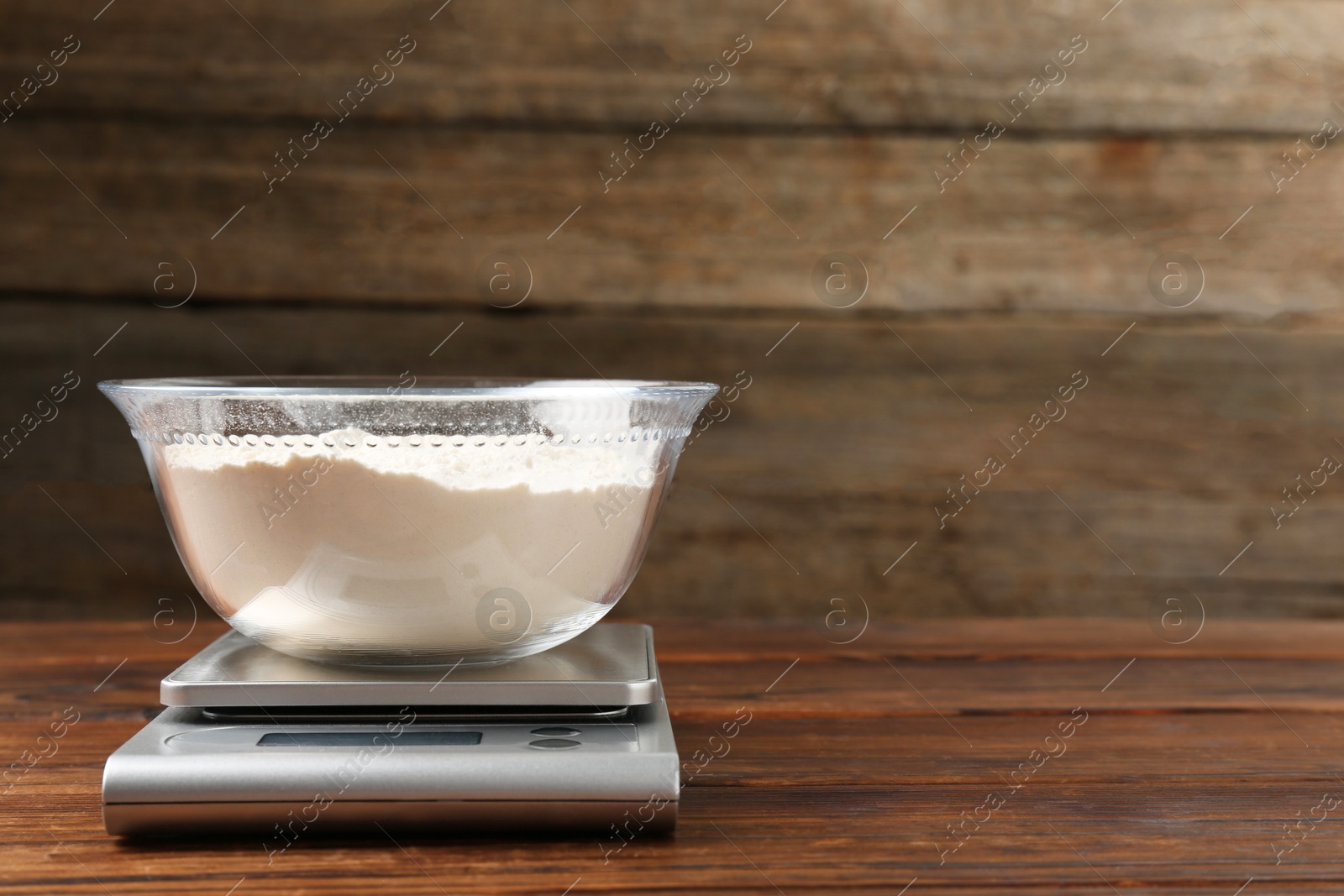 Photo of Electronic kitchen scale with bowl of flour on wooden table, closeup. Space for text