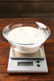 Photo of Electronic kitchen scale with bowl of flour on wooden table, closeup