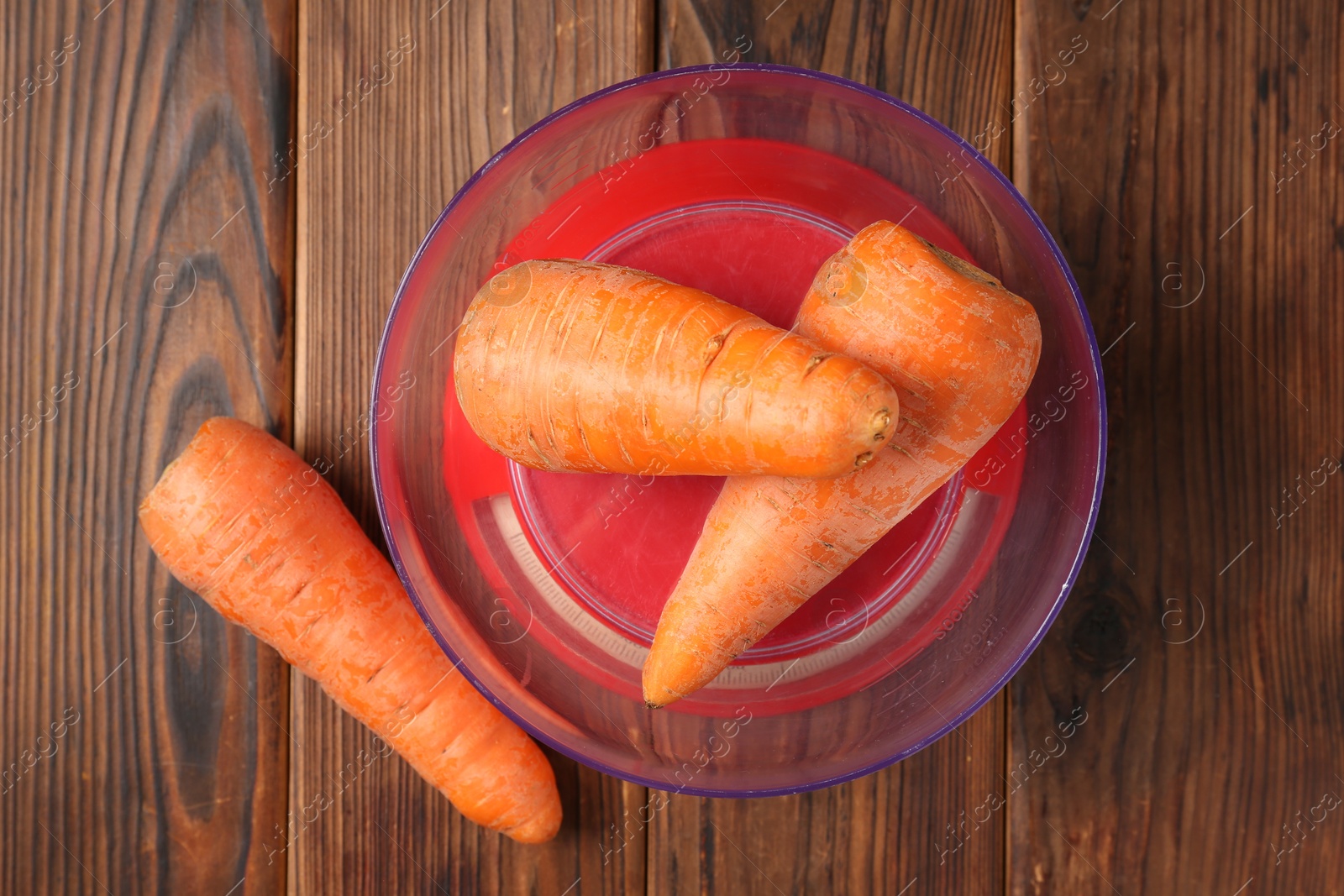 Photo of Kitchen scale with fresh carrots on wooden table, flat lay