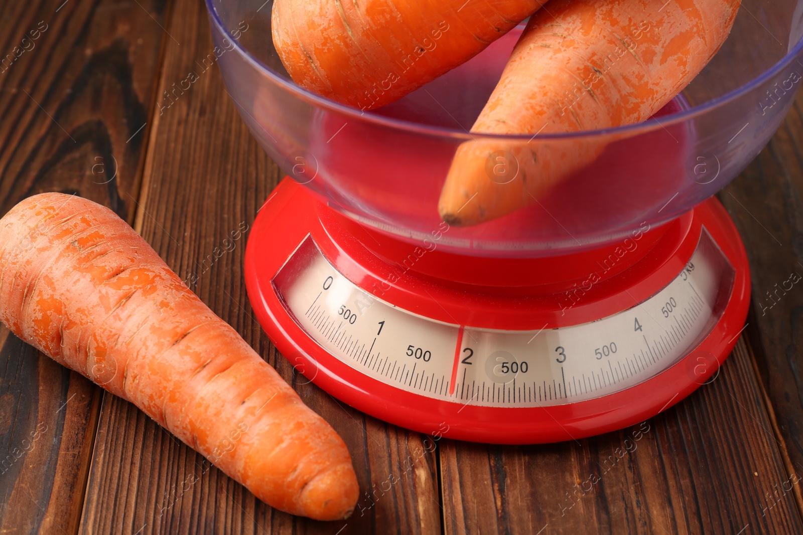 Photo of Kitchen scale with fresh carrots on wooden table, closeup