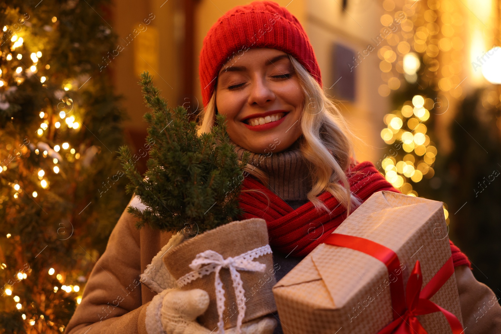 Photo of Happy woman with Christmas gift and thuja tree on city street