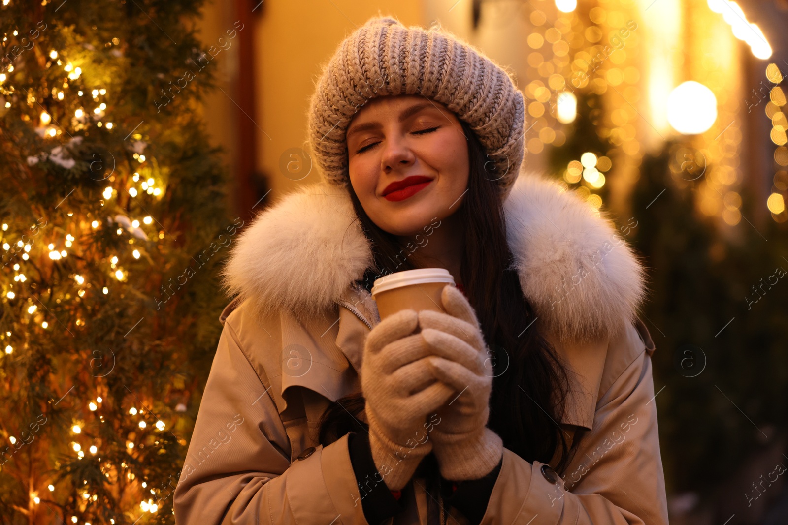 Photo of Happy woman with paper cup of coffee on city street. Christmas season