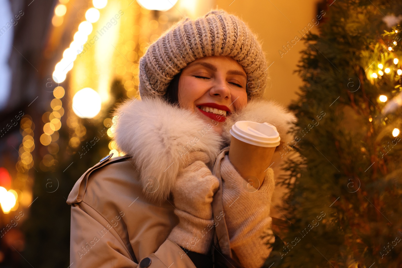 Photo of Happy woman with paper cup of coffee on city street. Christmas season