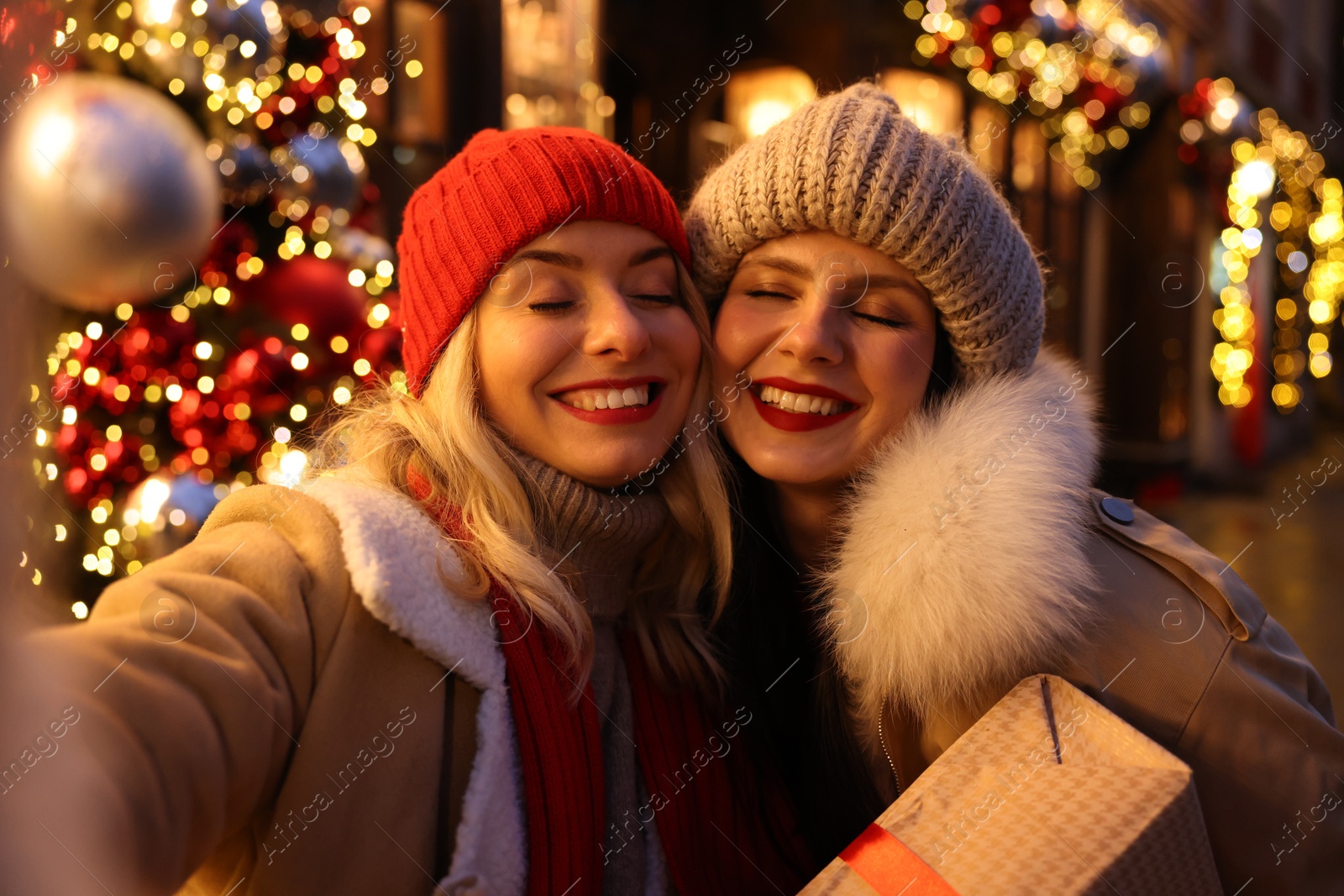 Photo of Happy friends with Christmas gift taking selfie on city street