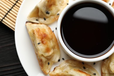 Photo of Delicious fried gyoza dumplings with sesame seeds and soy sauce on table, top view