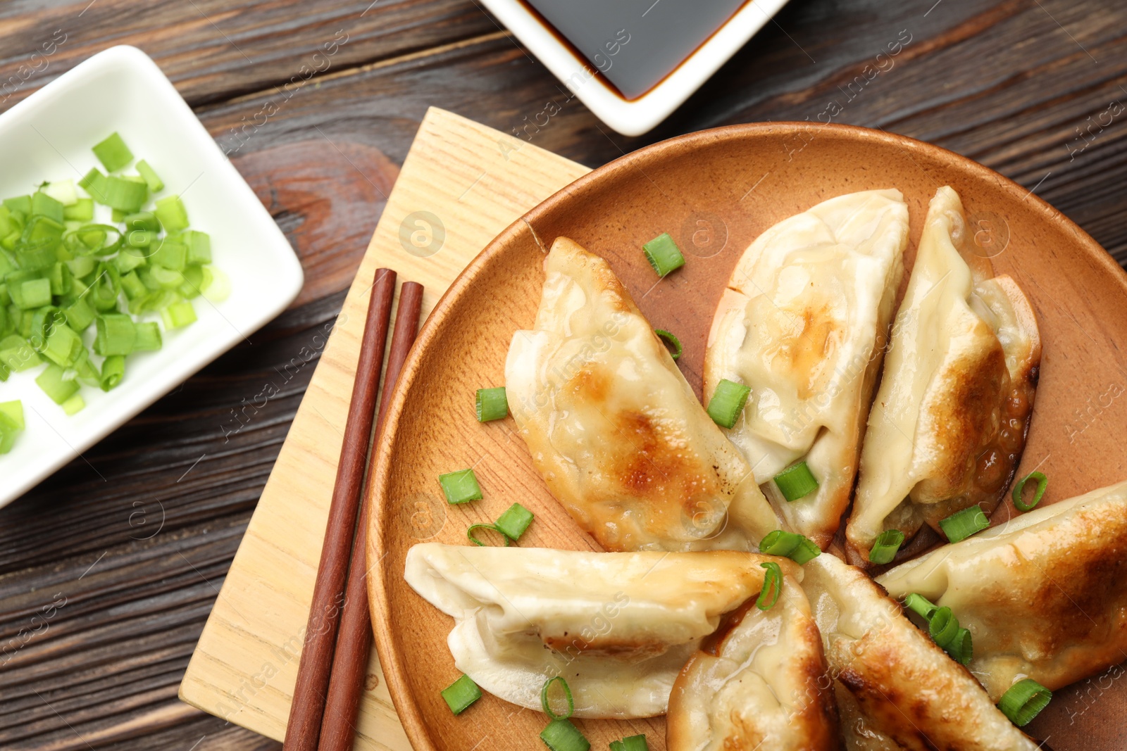 Photo of Delicious fried gyoza dumplings with green onions served on wooden table, flat lay