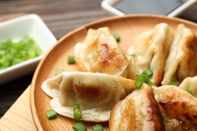 Photo of Delicious fried gyoza dumplings with green onions served on wooden table, closeup