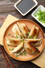 Photo of Delicious fried gyoza dumplings with green onions served on wooden table, flat lay