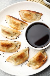 Photo of Fried gyoza dumplings with sesame seeds and soy sauce on table, top view