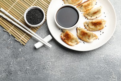 Photo of Delicious fried gyoza dumplings with sesame seeds served on grey table, flat lay. Space for text