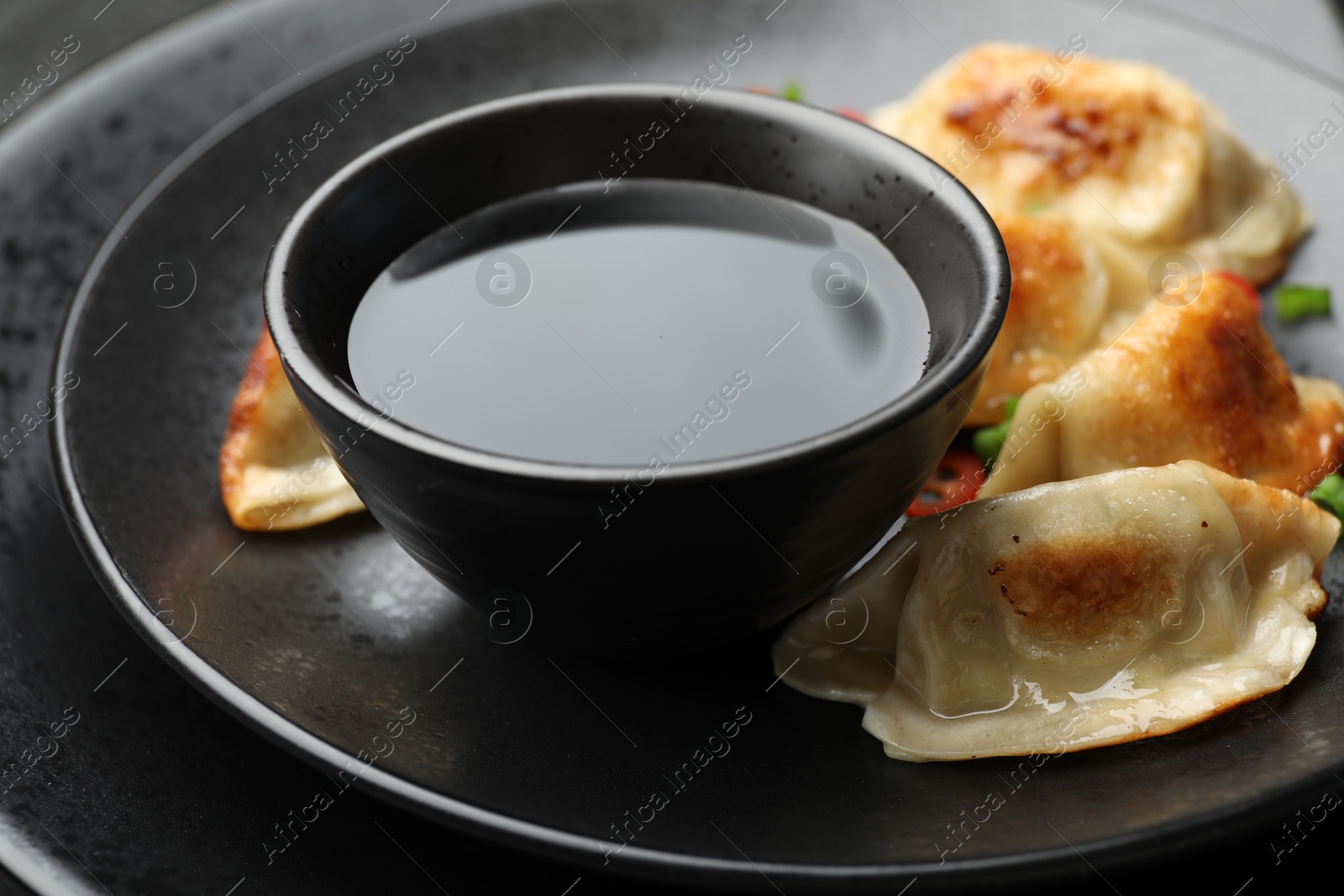 Photo of Fried gyoza dumplings with soy sauce on black table, closeup