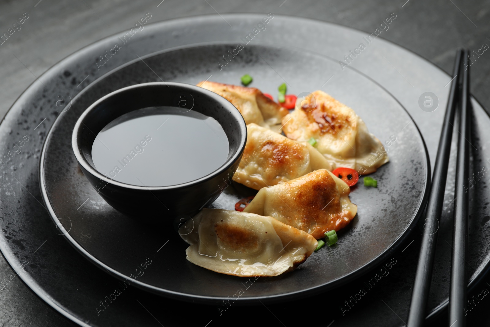 Photo of Delicious fried gyoza dumplings with green onions and chili peppers served on black table, closeup