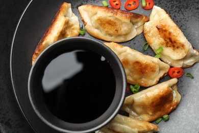 Photo of Fried gyoza dumplings with green onions, chili peppers and soy sauce on black table, top view