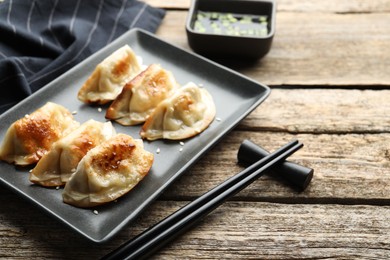 Photo of Delicious fried gyoza dumplings with sesame seeds served on wooden table, closeup