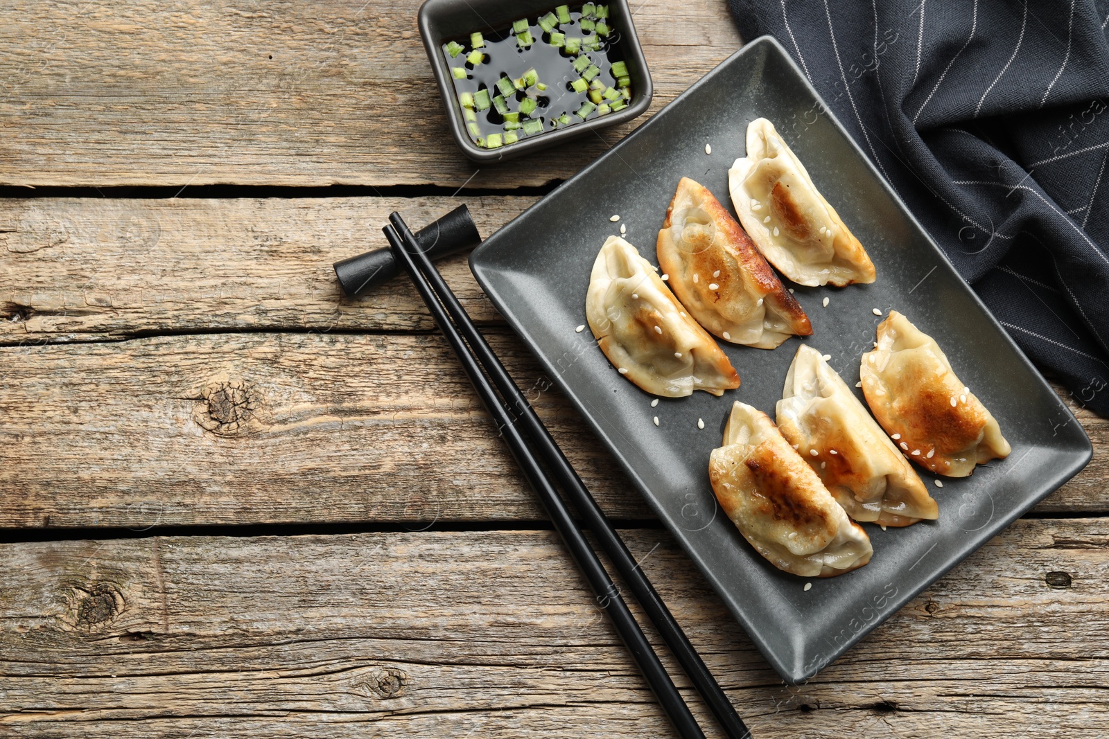 Photo of Delicious fried gyoza dumplings with sesame seeds served on wooden table, flat lay. Space for text