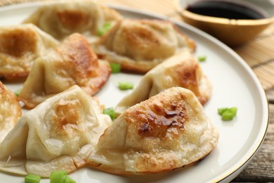 Photo of Delicious fried gyoza dumplings with green onions served on wooden table, closeup