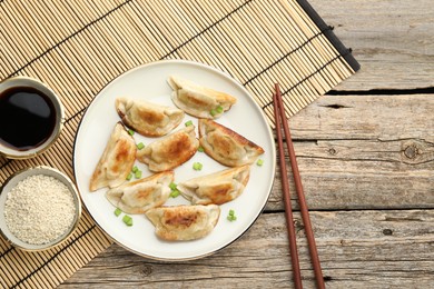 Photo of Delicious fried gyoza dumplings with green onions served on wooden table, flat lay