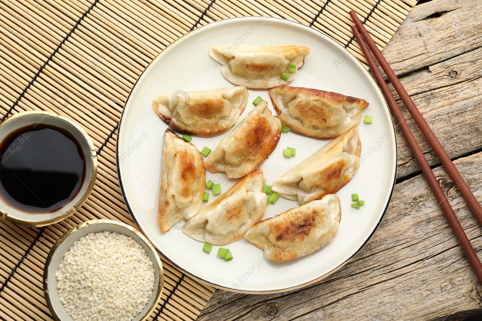 Photo of Delicious fried gyoza dumplings with green onions served on wooden table, flat lay