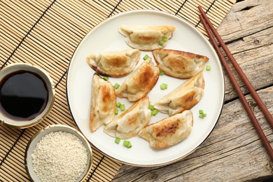 Photo of Delicious fried gyoza dumplings with green onions served on wooden table, flat lay