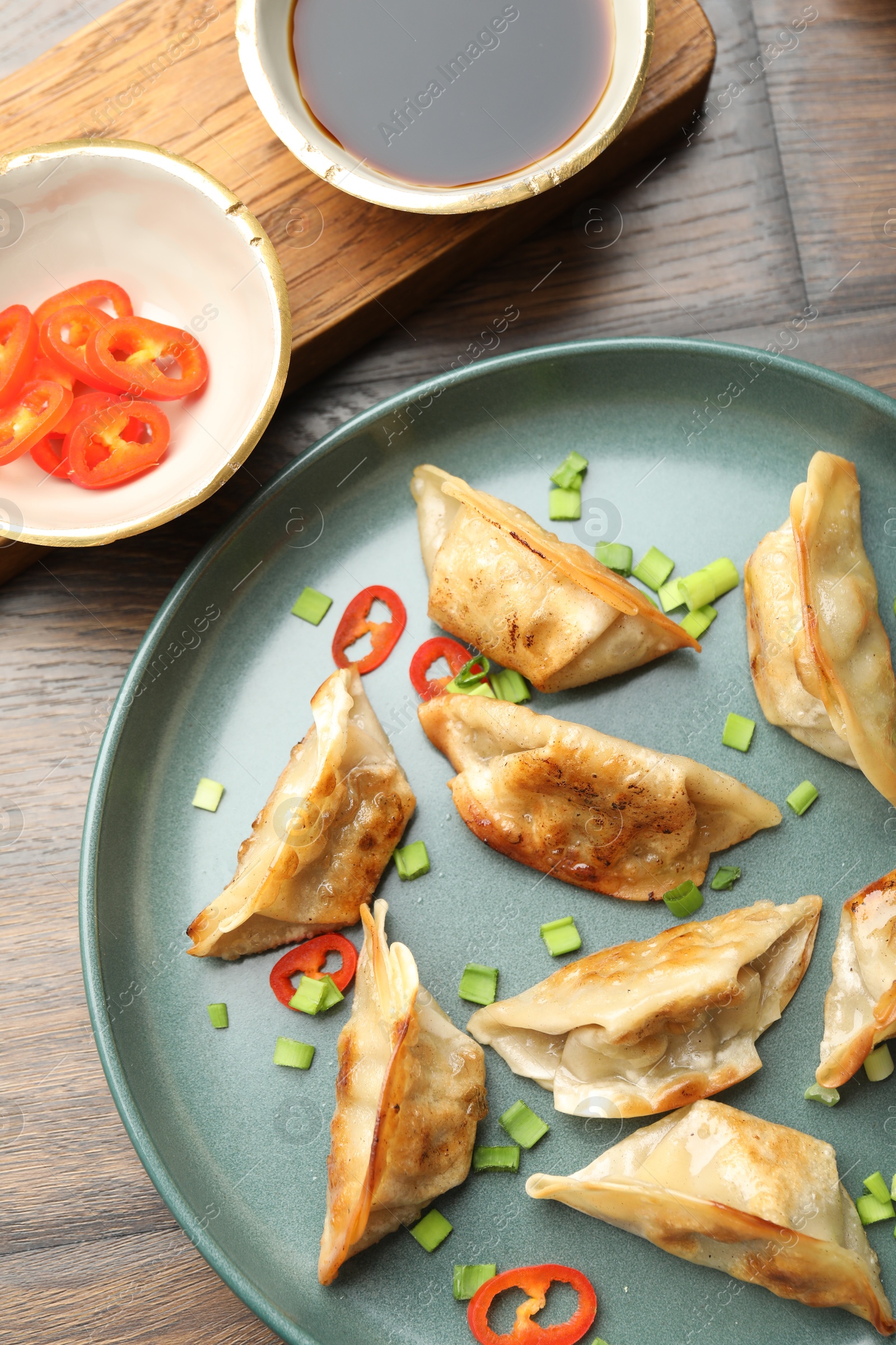 Photo of Delicious fried gyoza dumplings with green onions and chili peppers served on wooden table, flat lay