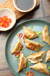 Photo of Delicious fried gyoza dumplings with green onions and chili peppers served on wooden table, flat lay