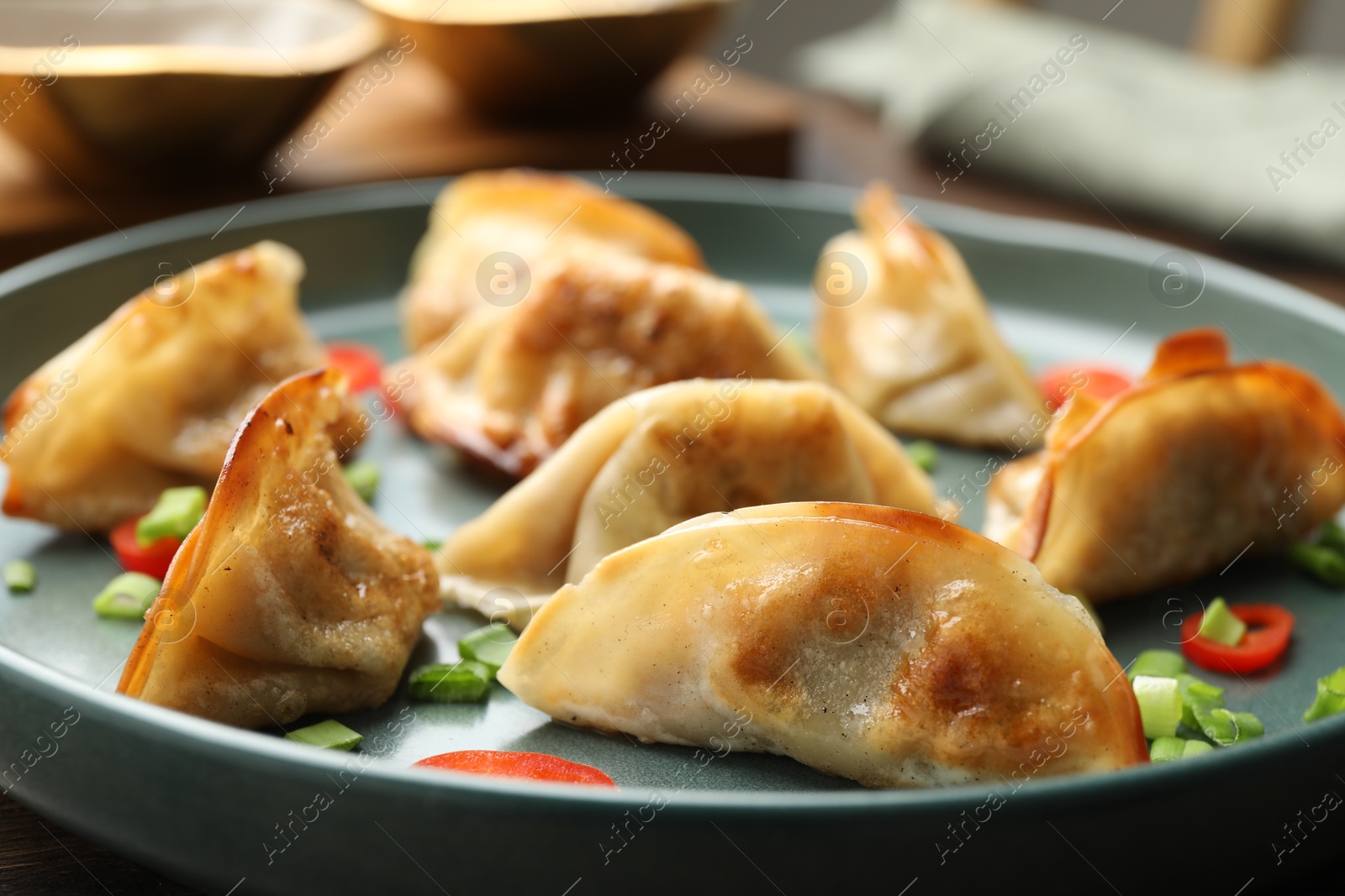 Photo of Fried gyoza dumplings with green onions and chili peppers on table, closeup