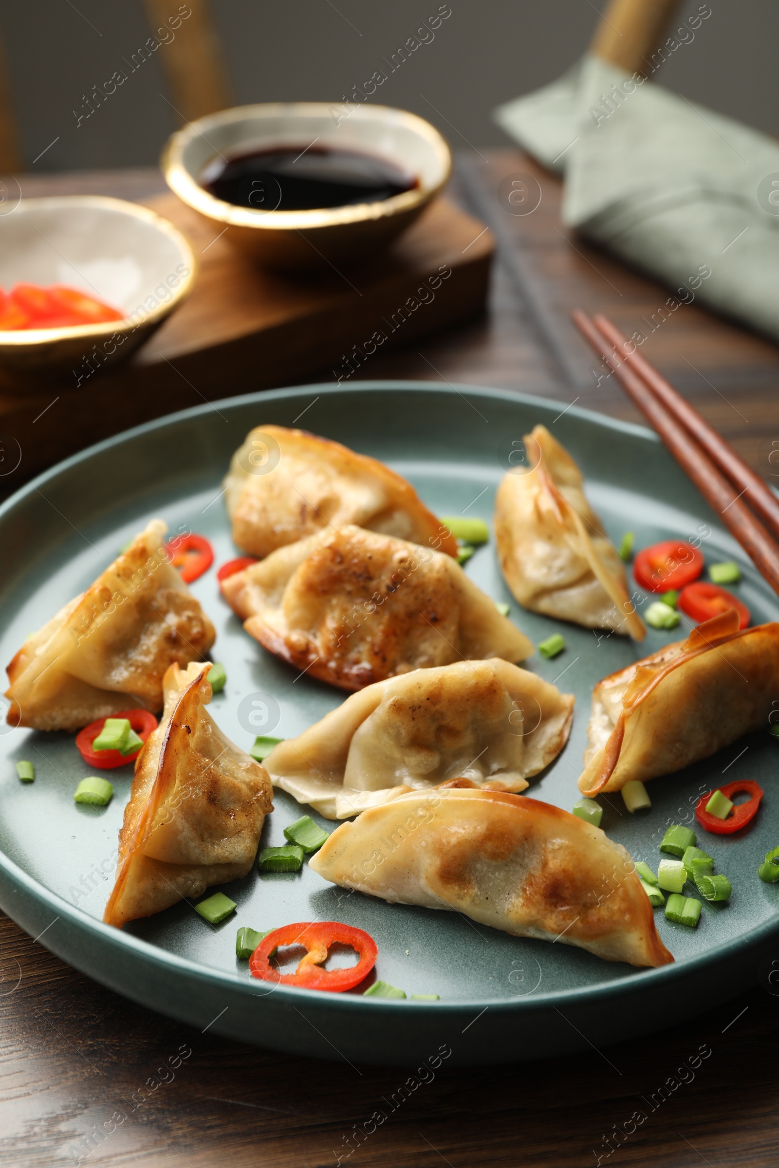 Photo of Delicious fried gyoza dumplings with green onions and chili peppers served on wooden table, closeup