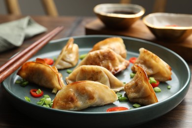 Photo of Delicious fried gyoza dumplings with green onions and chili peppers served on wooden table, closeup