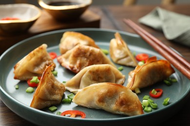 Photo of Delicious fried gyoza dumplings with green onions and chili peppers served on wooden table, closeup