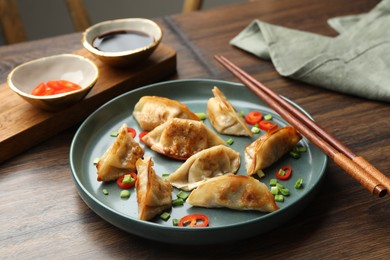 Photo of Delicious fried gyoza dumplings with green onions and chili peppers served on wooden table, closeup