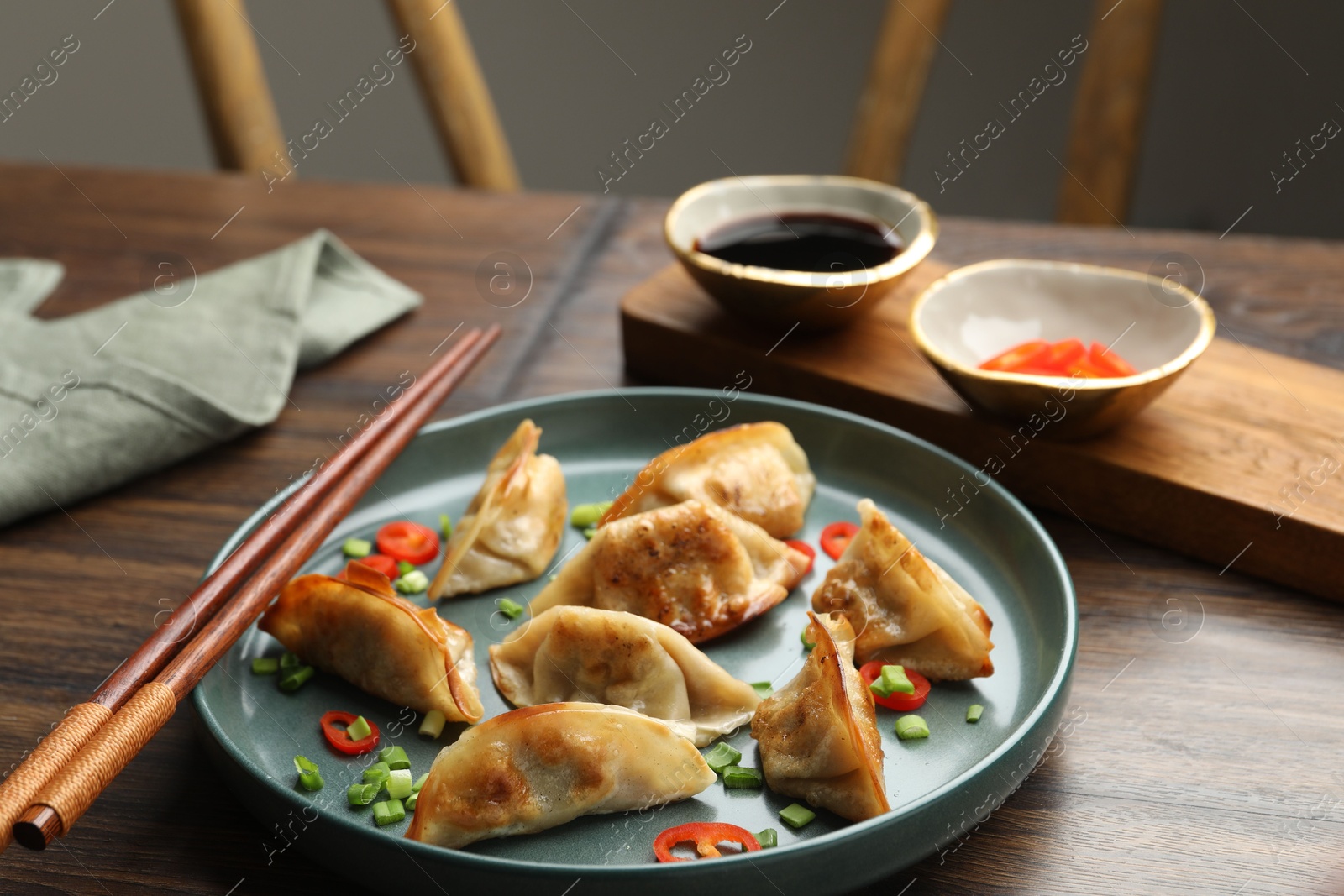 Photo of Delicious fried gyoza dumplings with green onions and chili peppers served on wooden table, closeup