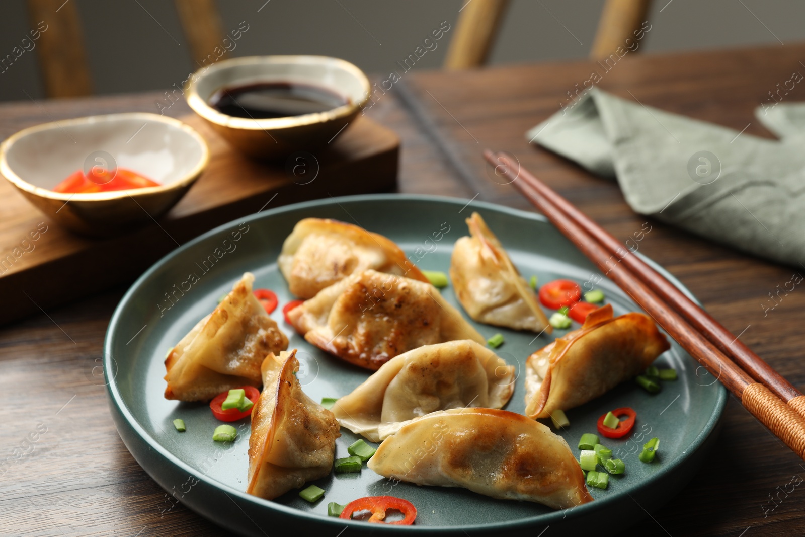 Photo of Delicious fried gyoza dumplings with green onions and chili peppers served on wooden table, closeup