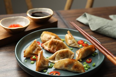 Delicious fried gyoza dumplings with green onions and chili peppers served on wooden table, closeup