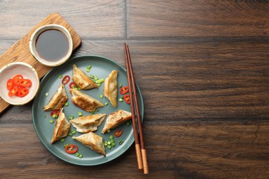 Photo of Delicious fried gyoza dumplings with green onions and chili peppers served on wooden table, flat lay. Space for text