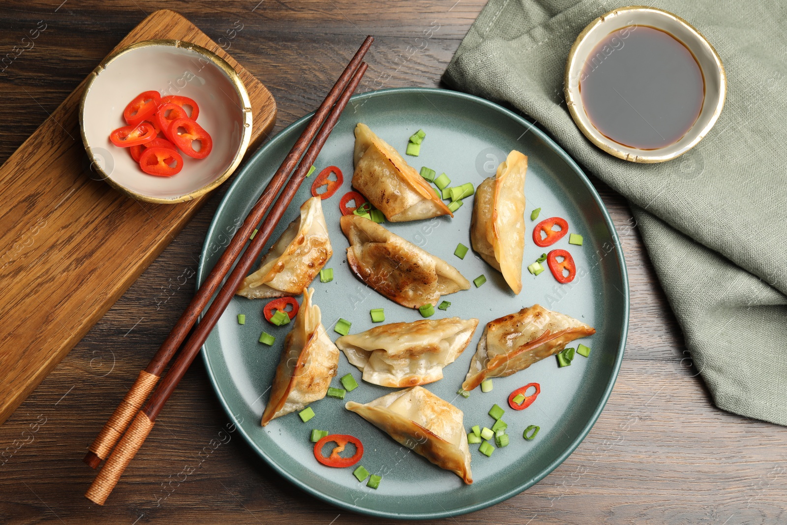 Photo of Delicious fried gyoza dumplings with green onions and chili peppers served on wooden table, flat lay