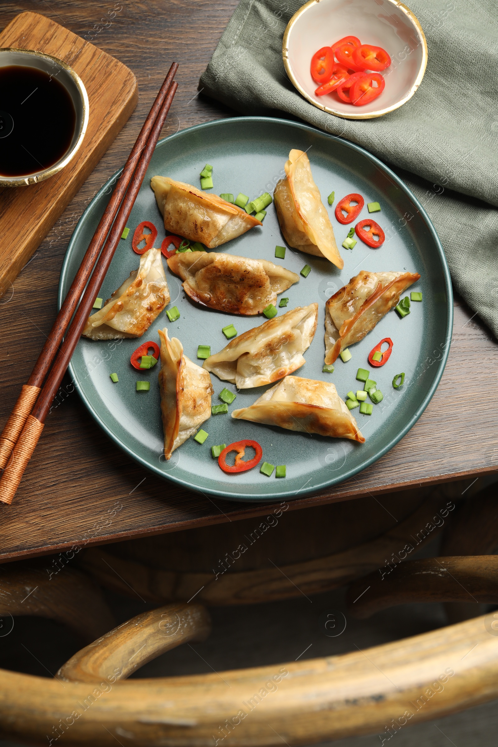 Photo of Delicious fried gyoza dumplings with green onions and chili peppers served on wooden table, flat lay