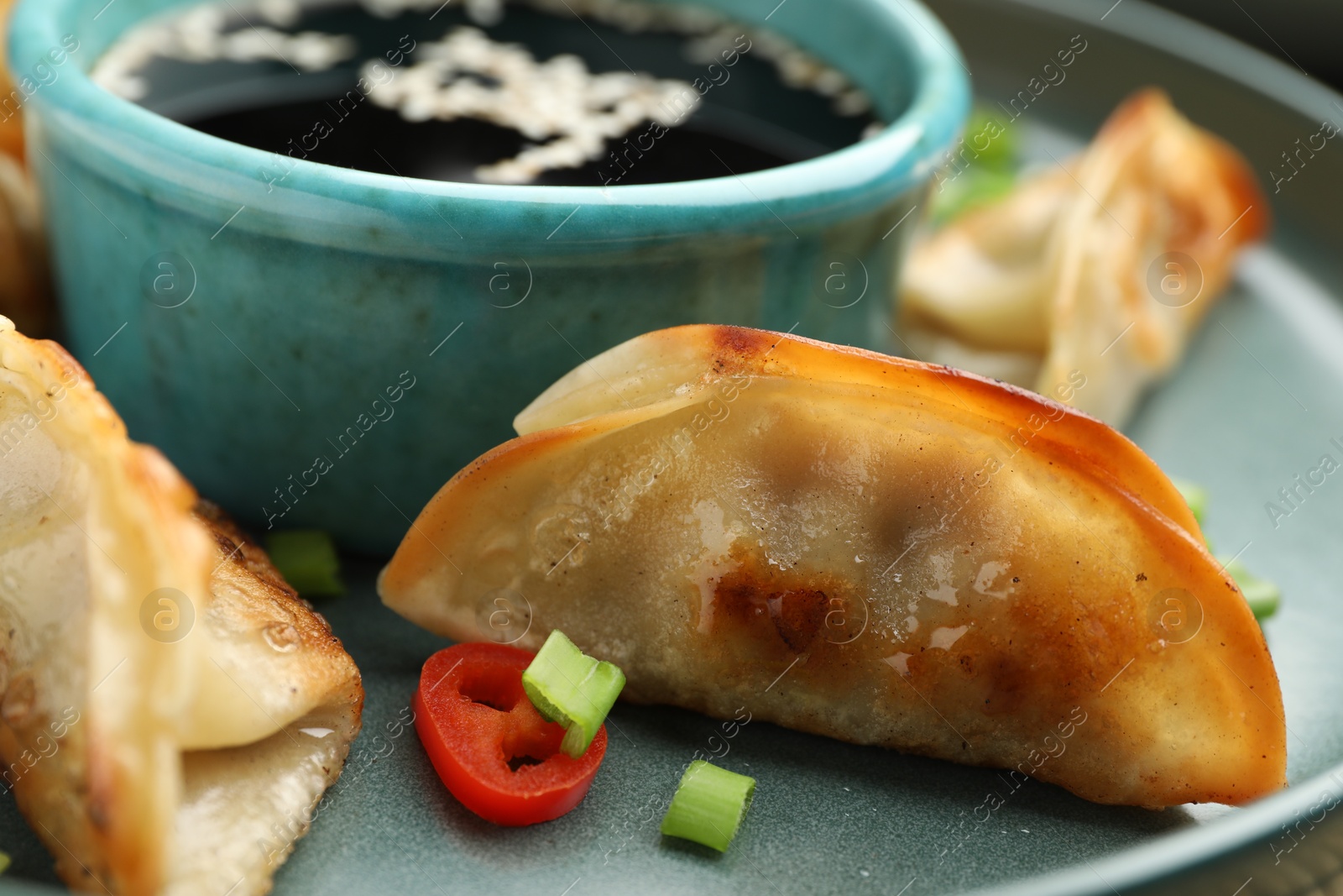 Photo of Fried gyoza dumplings with green onions, chili peppers and soy sauce on table, closeup