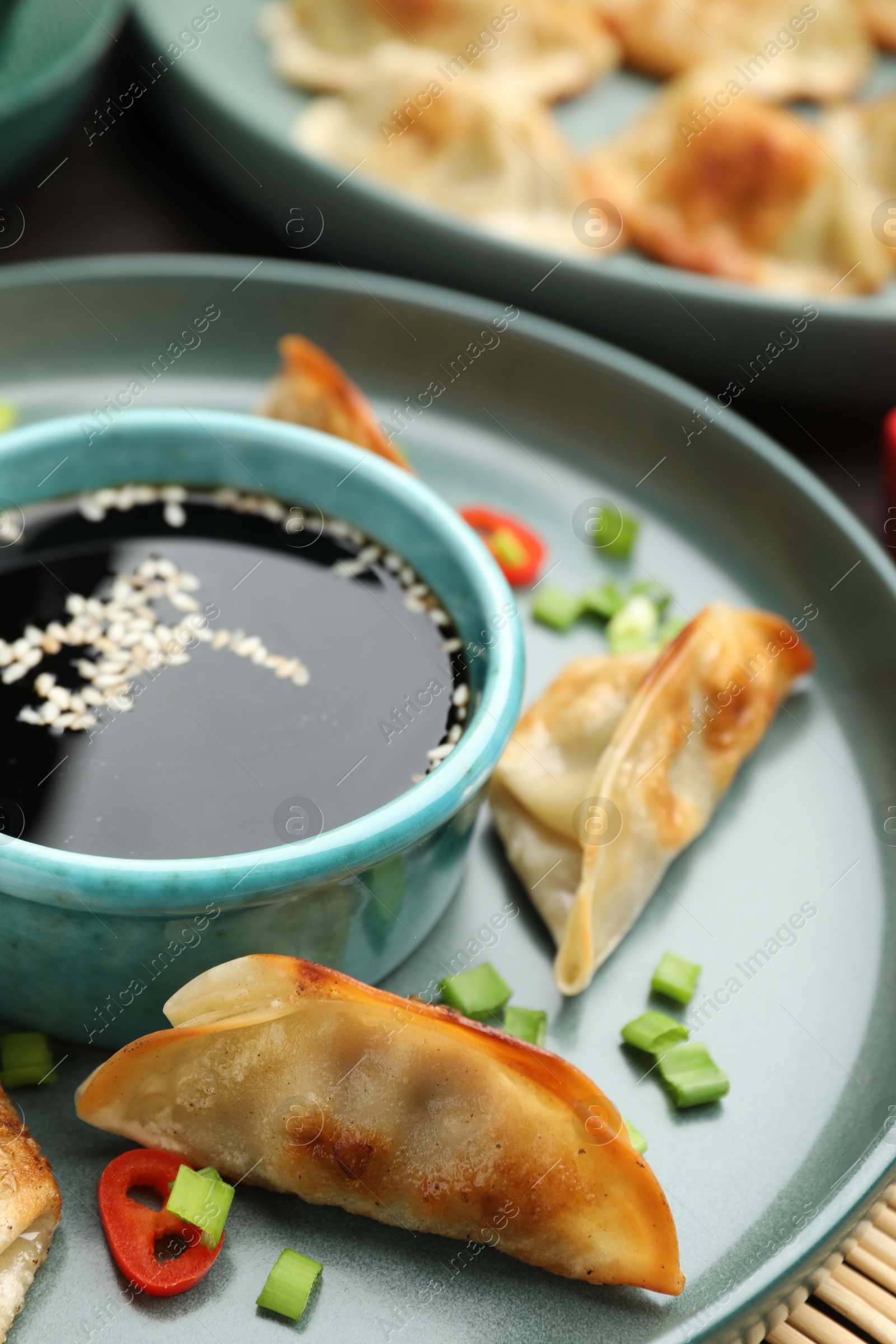 Photo of Fried gyoza dumplings with green onions, chili peppers and soy sauce on table, closeup