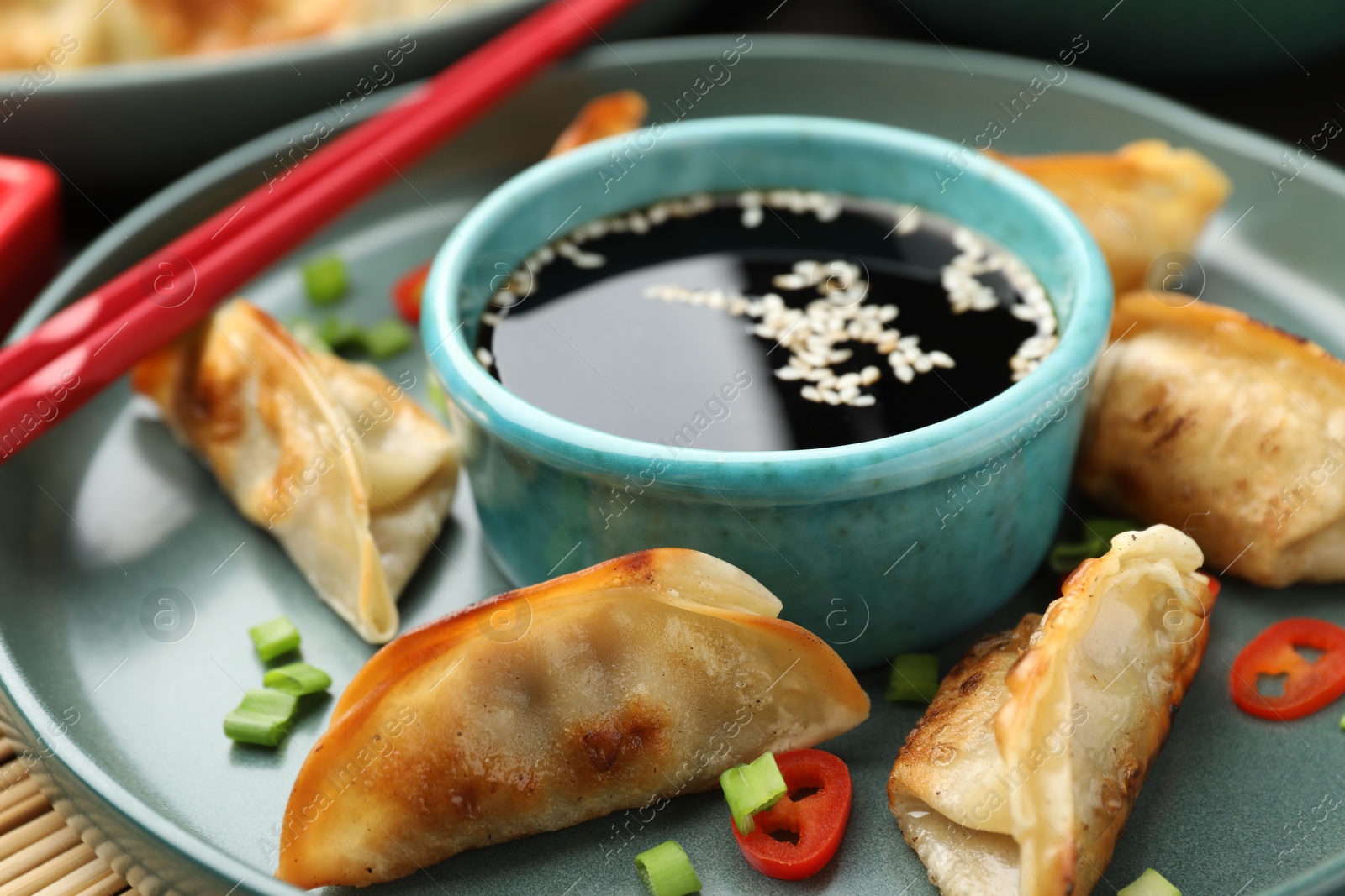 Photo of Delicious fried gyoza dumplings with green onions and chili peppers served on table, closeup