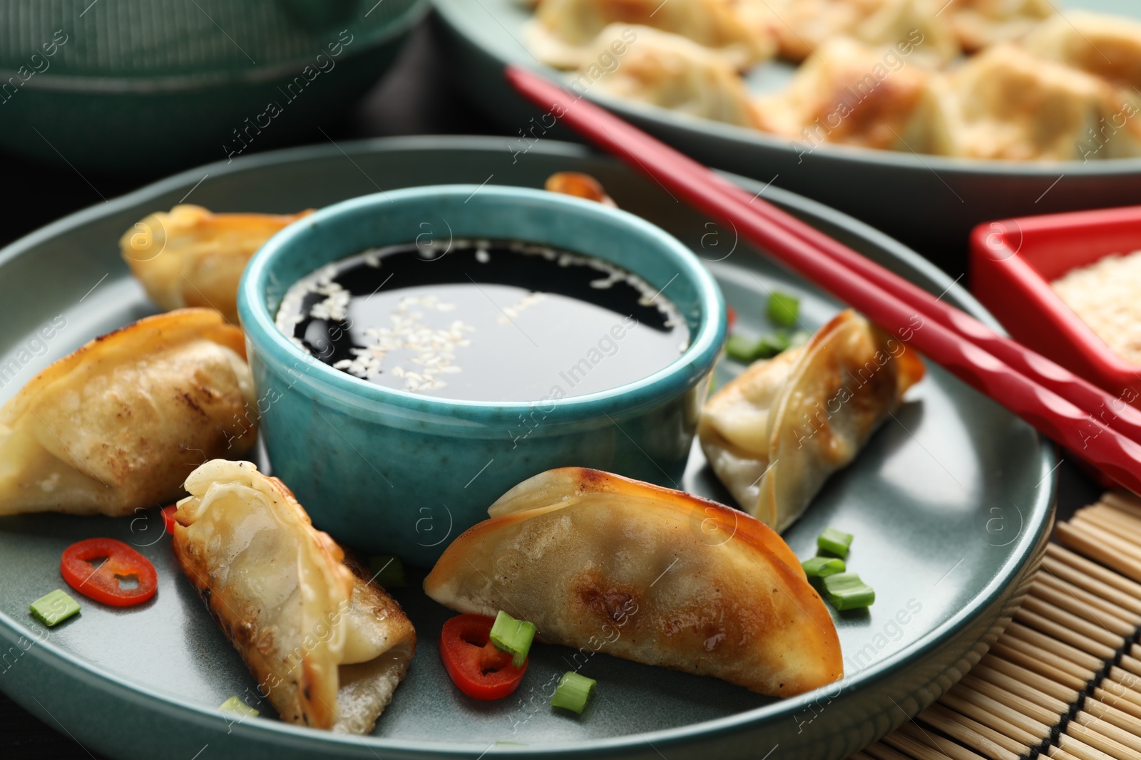 Photo of Delicious fried gyoza dumplings with green onions and chili peppers served on table, closeup