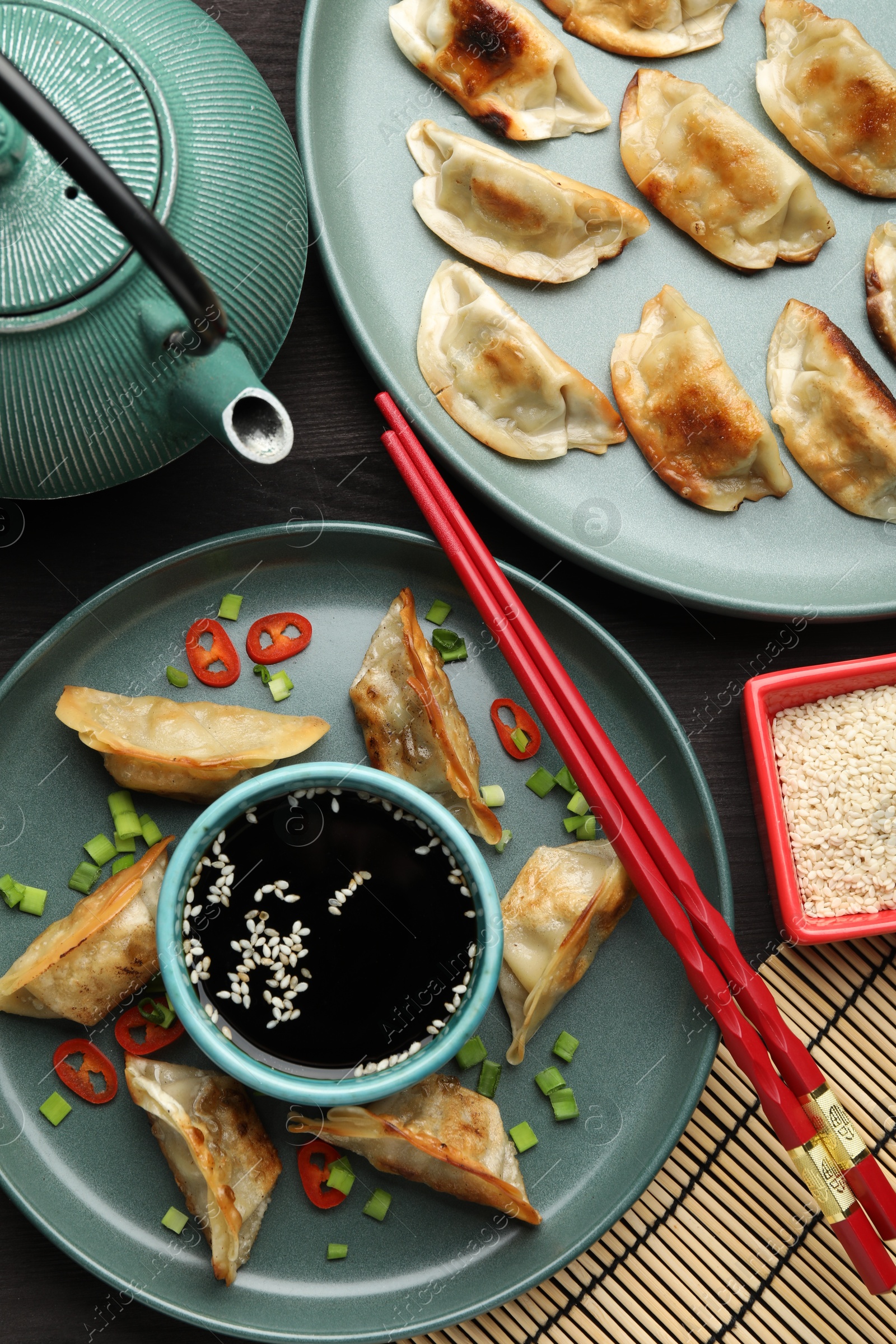 Photo of Delicious fried gyoza dumplings with green onions and chili peppers served on table, flat lay