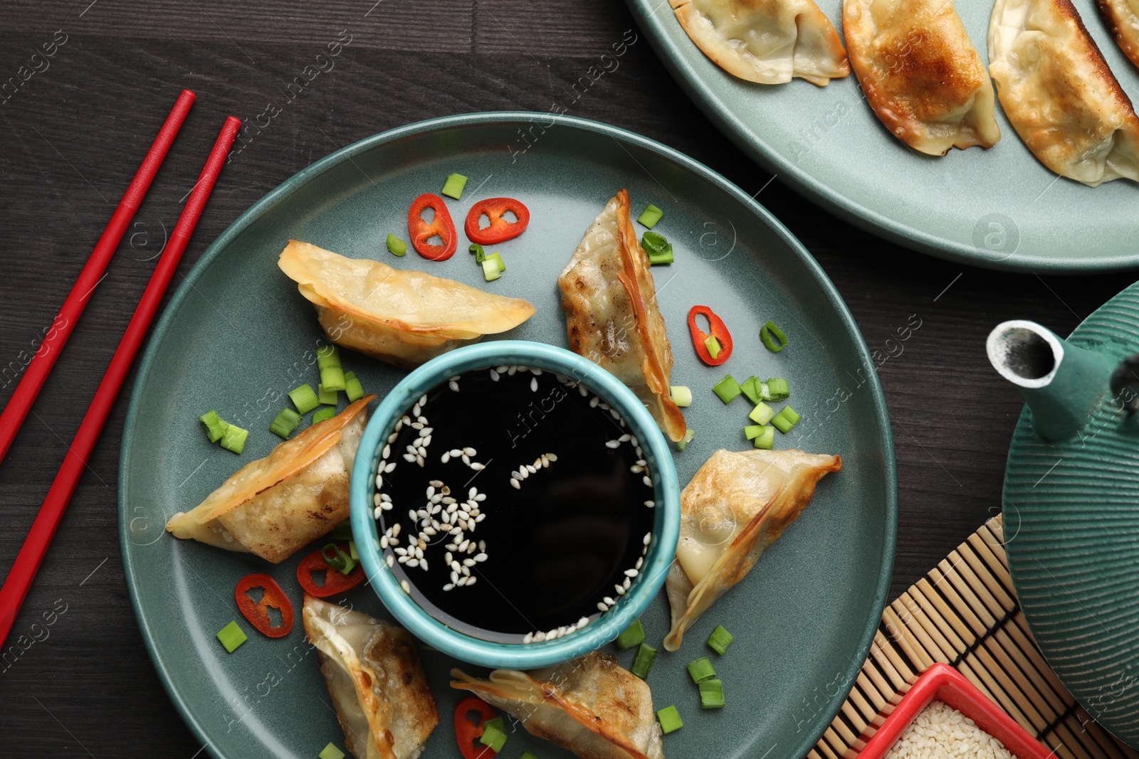 Photo of Delicious fried gyoza dumplings with green onions and chili peppers served on wooden table, flat lay