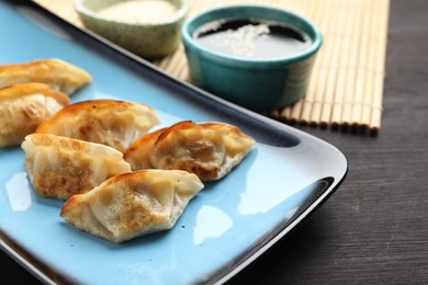 Photo of Fried gyoza dumplings and soy sauce on wooden table, closeup