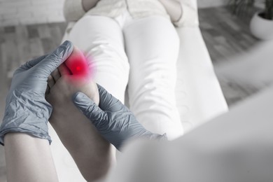 Image of Joint inflammation. Doctor checking woman's foot at hospital, closeup. Toned in black-and-white with color area on toe