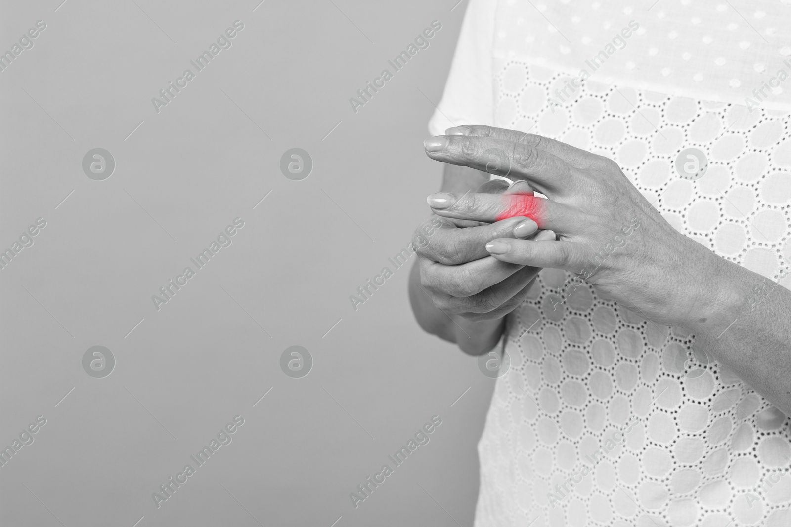 Image of Woman with joint inflammation on grey background, closeup. Toned in black-and-white with color area on finger