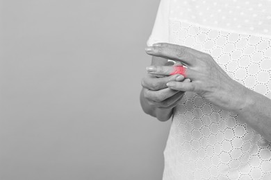 Image of Woman with joint inflammation on grey background, closeup. Toned in black-and-white with color area on finger