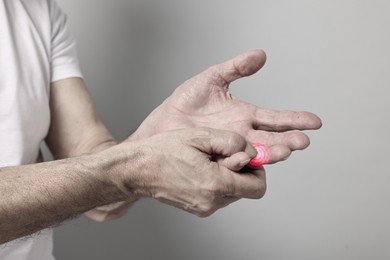 Image of Man with joint inflammation on grey background, closeup. Toned in black-and-white with color area on finger