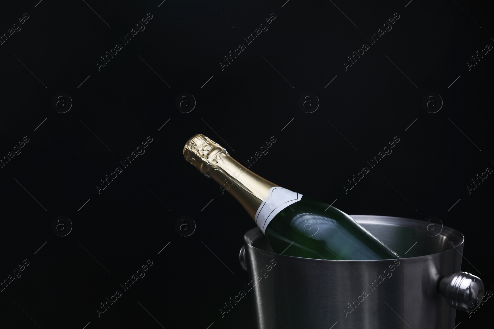 Photo of Bottle of champagne in bucket on black background, space for text