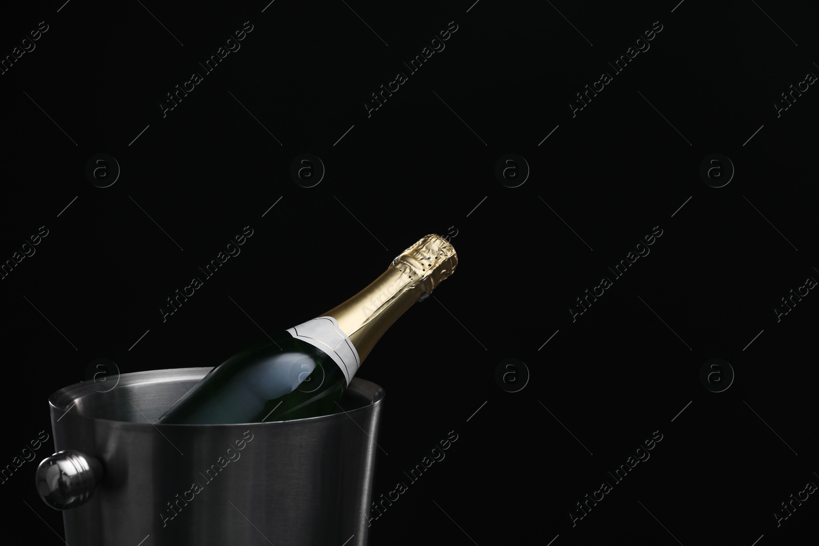 Photo of Bottle of champagne in bucket on black background, space for text